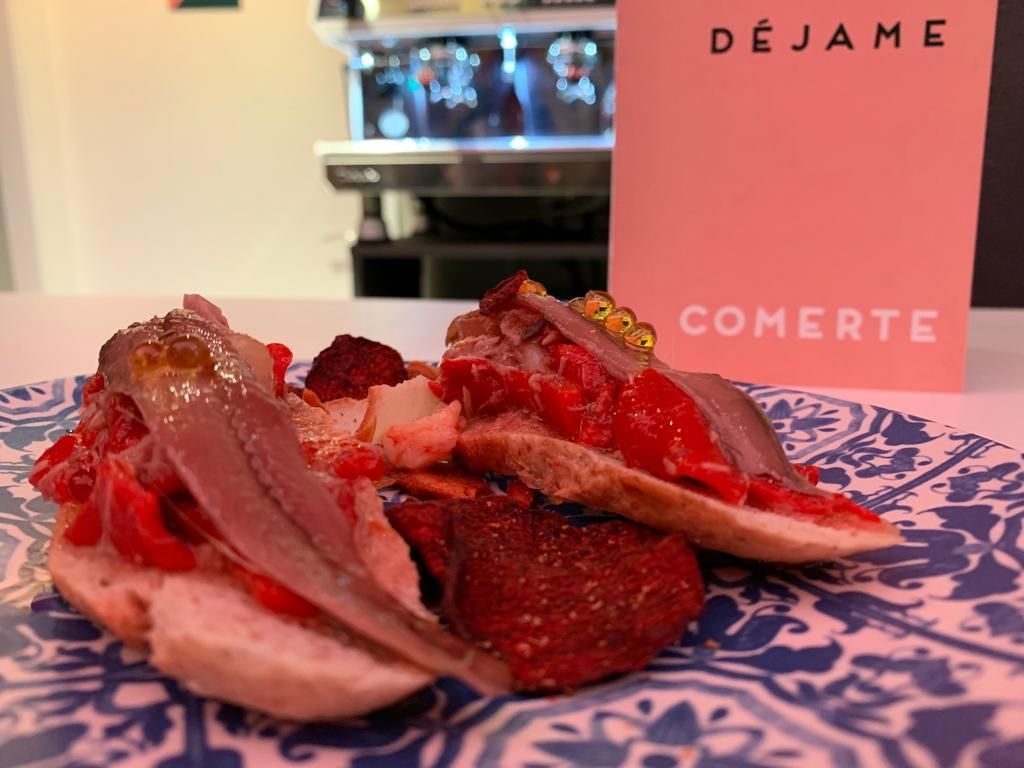 A plate of food with various meats and vegetables, a pink sign with "DÉJAME" and "COMERTE" text, and a blurred background with a counter.
