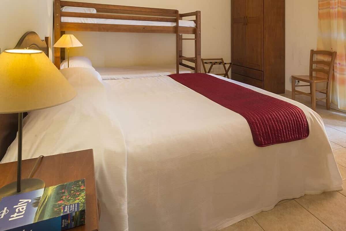 A single bed with a wooden headboard, a bedside lamp, a red throw blanket, and a wooden wardrobe.