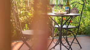 Una mesa con una botella de vino, dos copas y un plato de comida en un jardín.