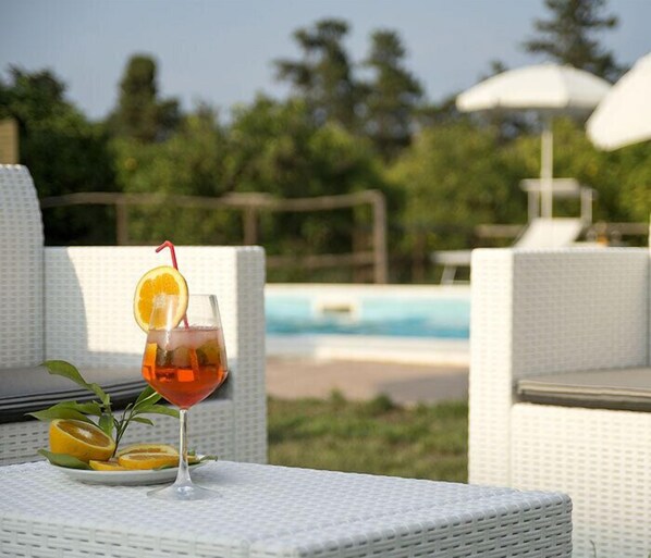 A glass of orange juice with a slice of orange and a straw on a table by a poolside. - Sicily Country House & Beach (Catania)