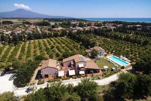 A residential area with a large house featuring a swimming pool and solar panels, surrounded by lush greenery and a view of a mountain and sea. - Sicily Country House & Beach (Catania)