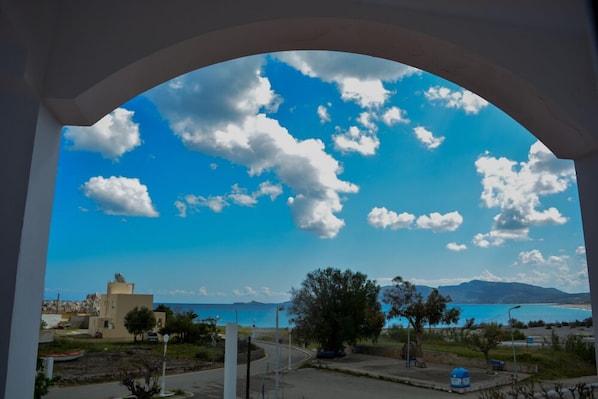 Vista a través de un arco de ventana a una zona costera, cielo despejado, una carretera y edificios a lo lejos.