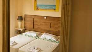 A bedroom with two beds, a nightstand, a lamp, and a painting of a beach scene. - Tommy's Rooms (Rhodes)