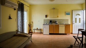 A compact living space with a sofa, a small table, a kitchenette with a refrigerator, and a cabinet above the counter. - Tommy's Rooms (Rhodes)