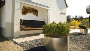 Un bâtiment blanc avec un banc en bois et un bac en métal contenant des plantes vertes.