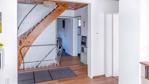 Un intérieur moderne avec un escalier en bois, un coin cuisine et un couloir menant à une autre pièce.