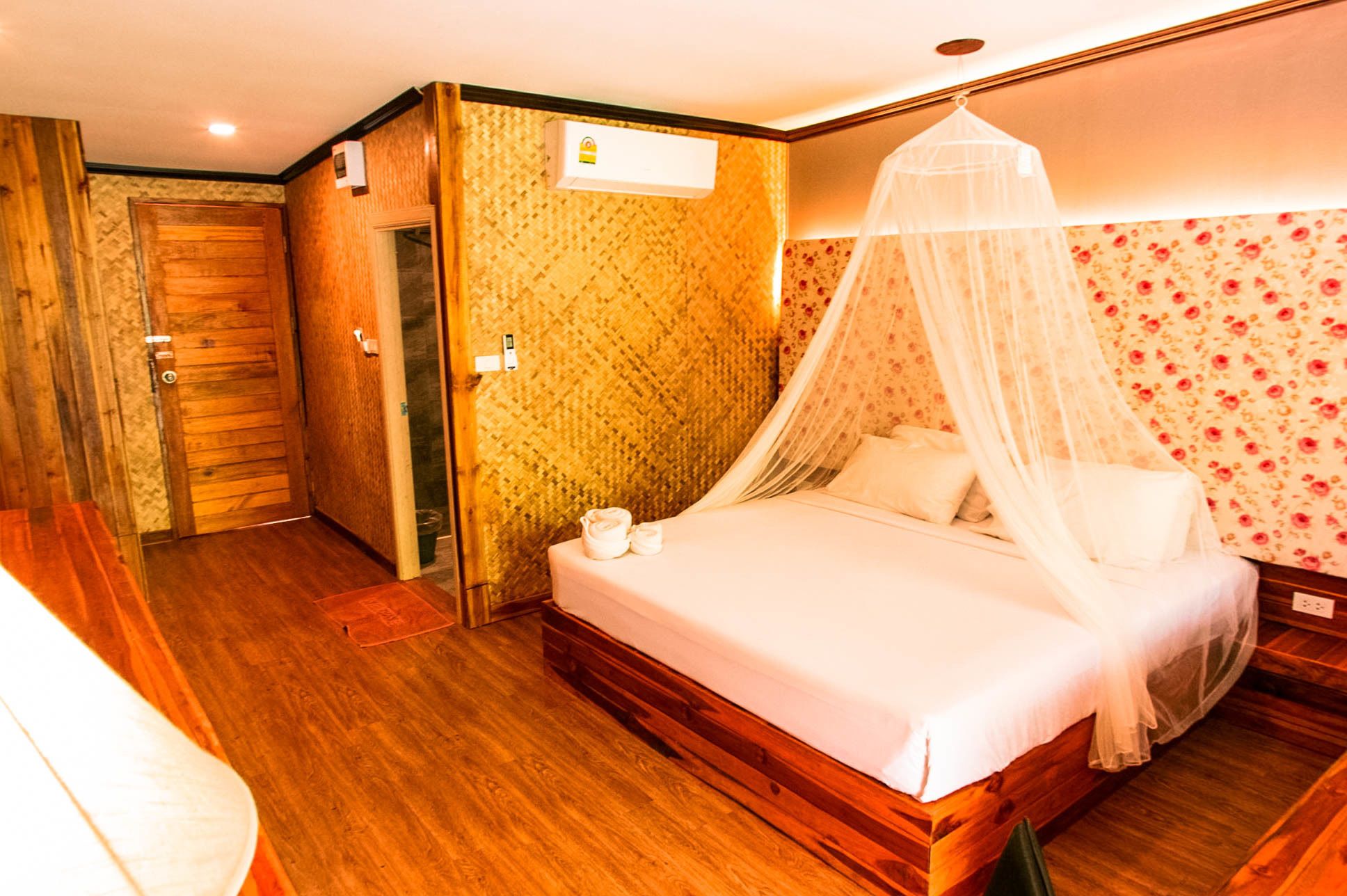 Ein Hotelzimmer mit Holzboden, einem Himmelsbett, einem kleinen Nachttisch und floralem Wandpapier.