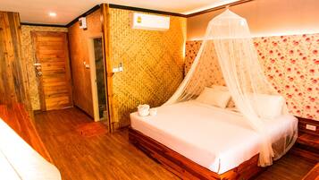 Ein Hotelzimmer mit Holzboden, einem Himmelsbett, einem kleinen Nachttisch und floralem Wandpapier.
