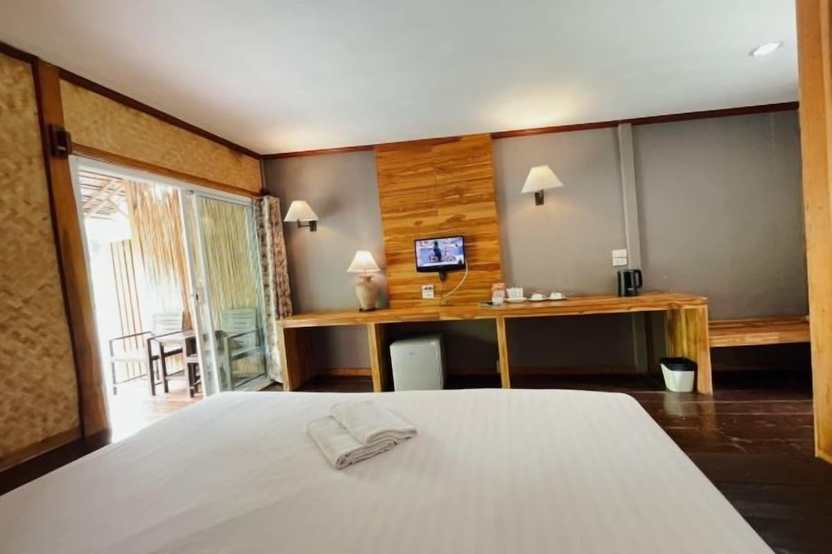 A hotel room with a large bed, a desk with a TV, and a view of the outside.