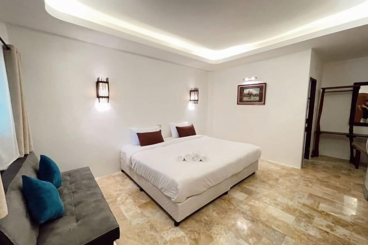 A bedroom with a bed, bedside lamps, a small table with chairs, and a picture on the wall.