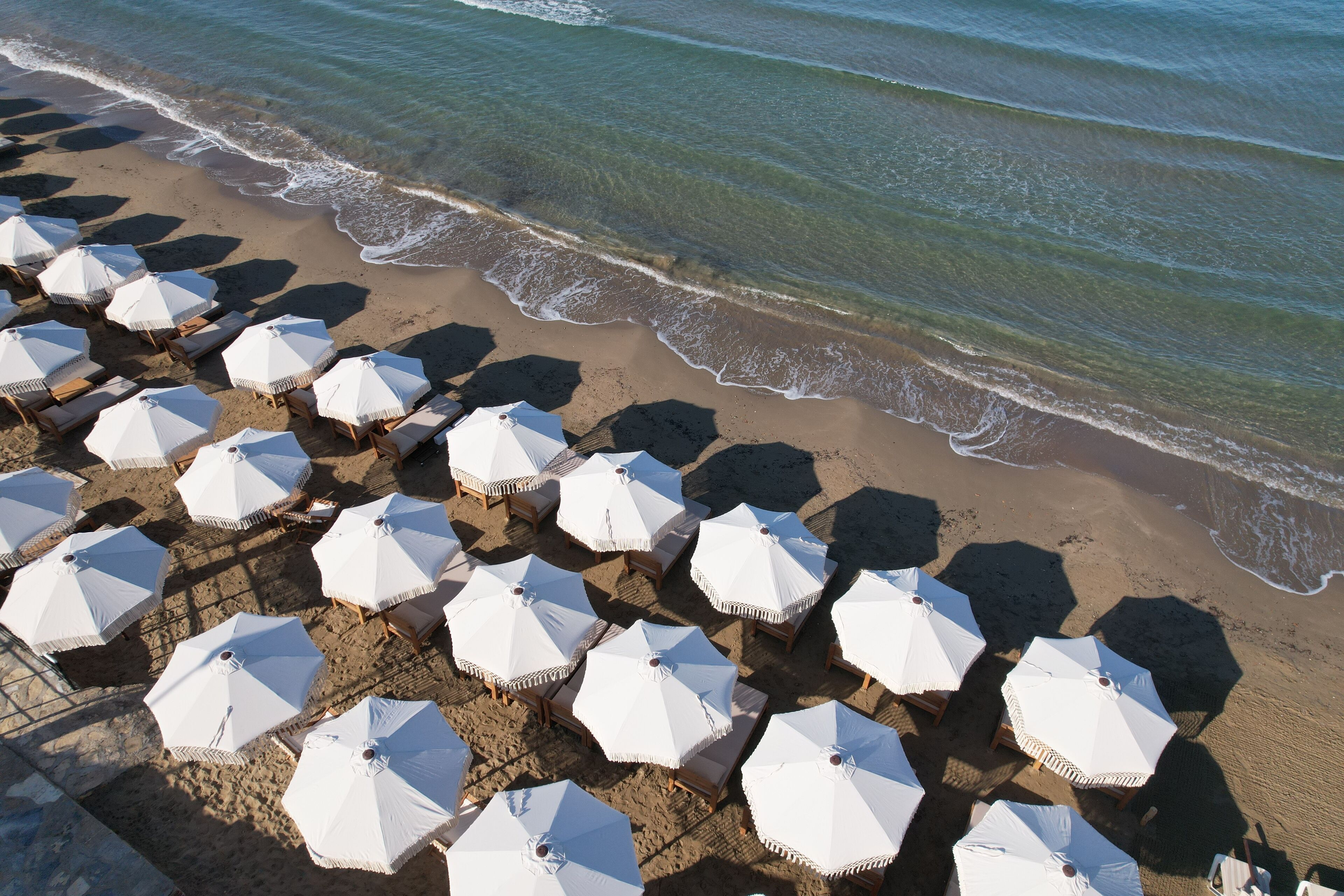 Een strand met rijen witte parasols en ligstoelen.