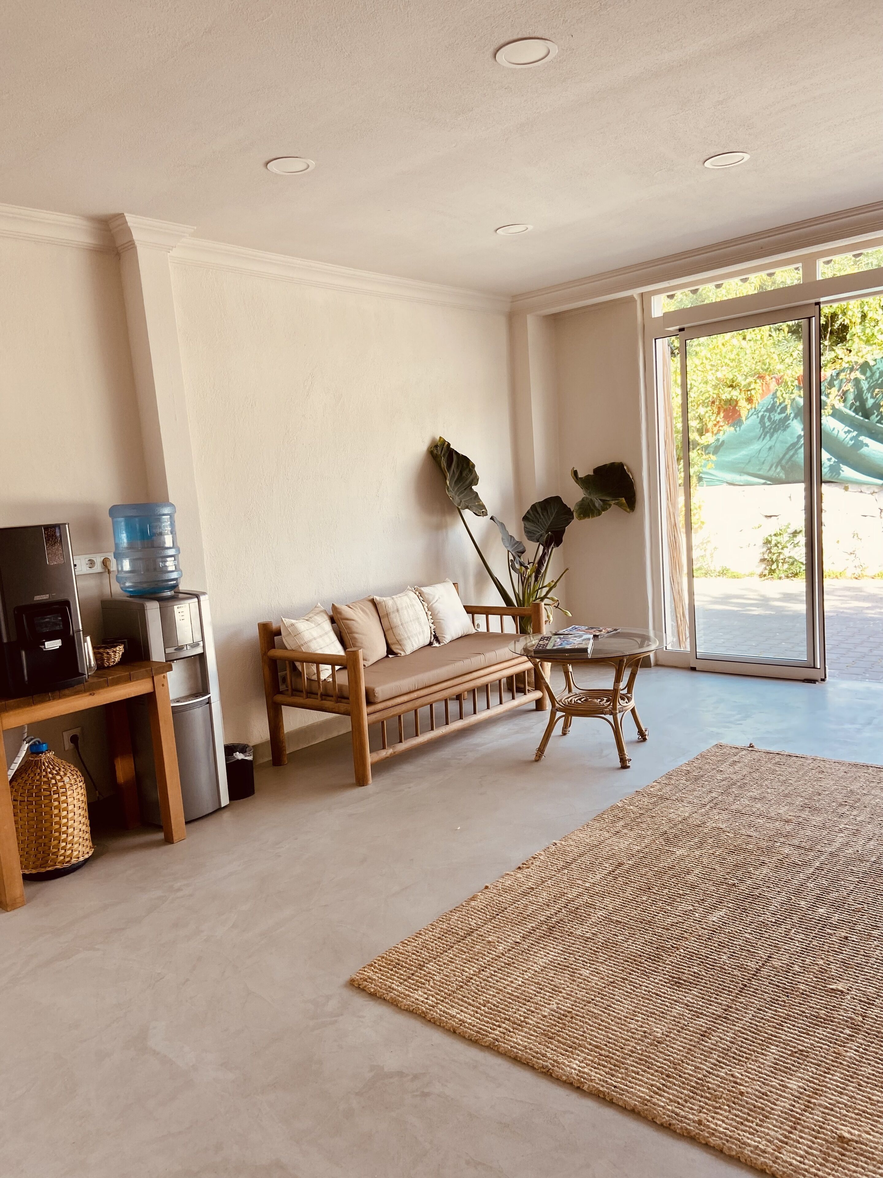 A living room with a sofa, a coffee table, a water dispenser, and a large window.