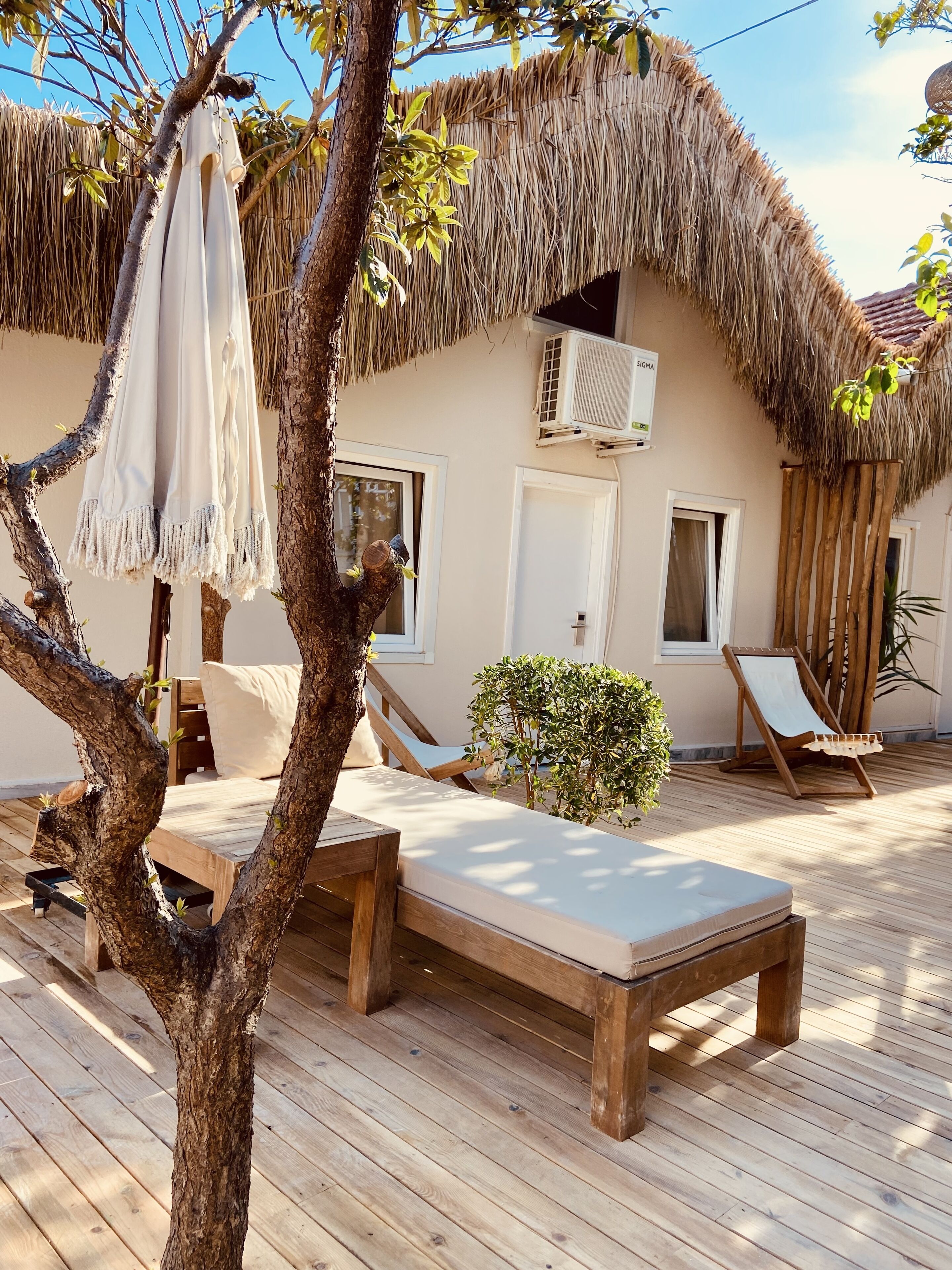 A wooden deck with a thatched roof, a lounge chair, a small table, and a potted plant.
