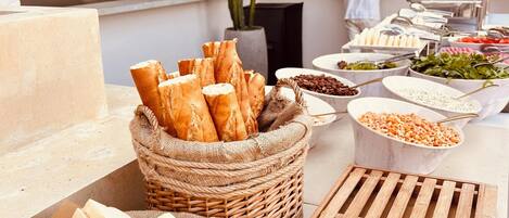 A buffet setup with various food items, including bread, salads, and other dishes, arranged on a table with a wooden slatted board.