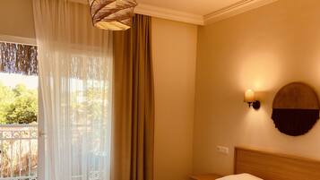 Quarto de hotel com uma cama grande, luminária pendente, abajur fixado na parede e vista pela janela com cortinas.