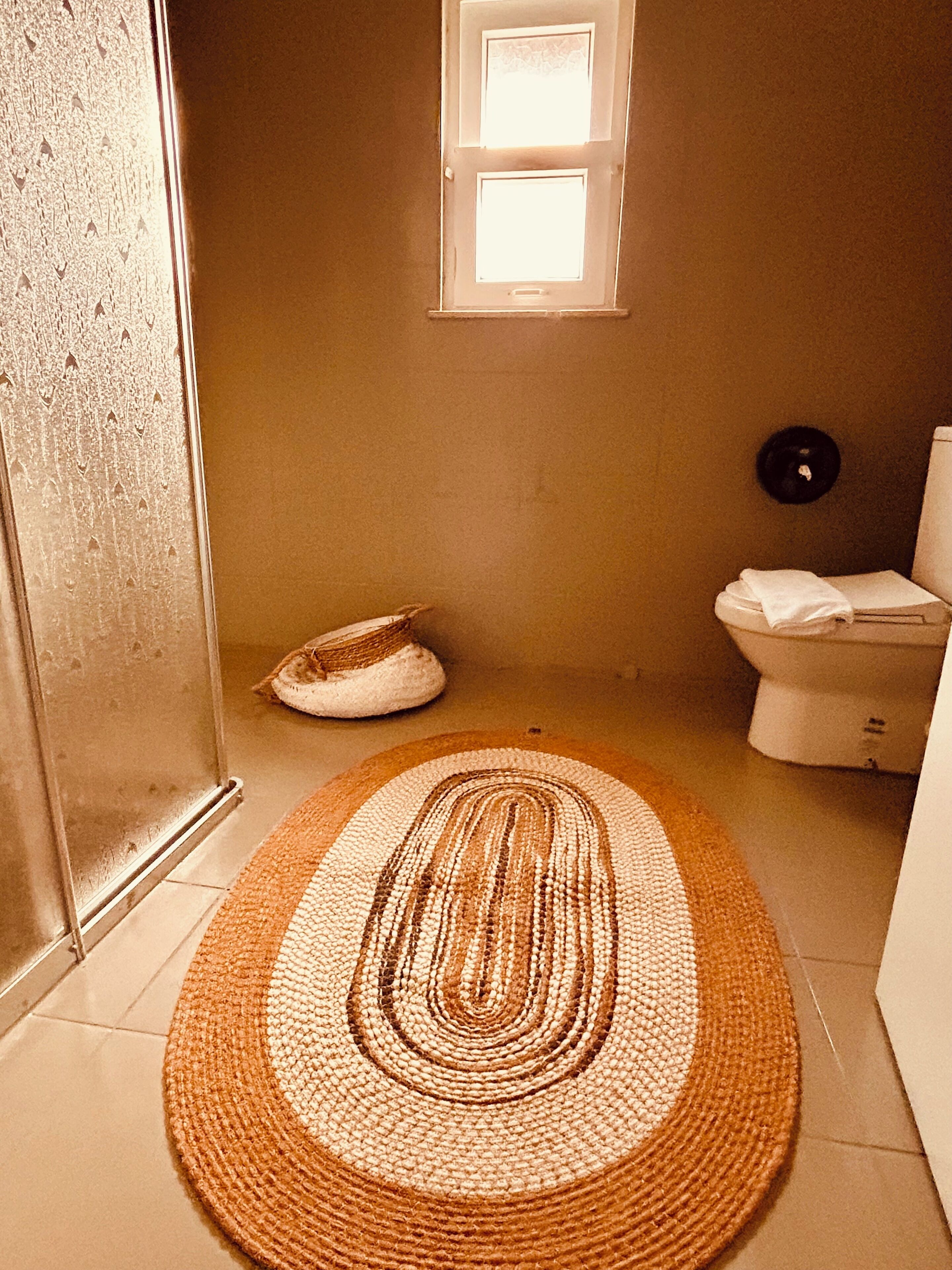 Un baño con un tapete redondo tejido, un inodoro y una pequeña ventana.
