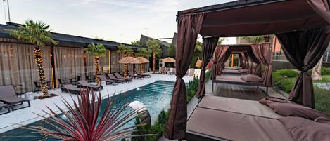 A poolside area with a canopy bed, lounge chairs, and a swimming pool.