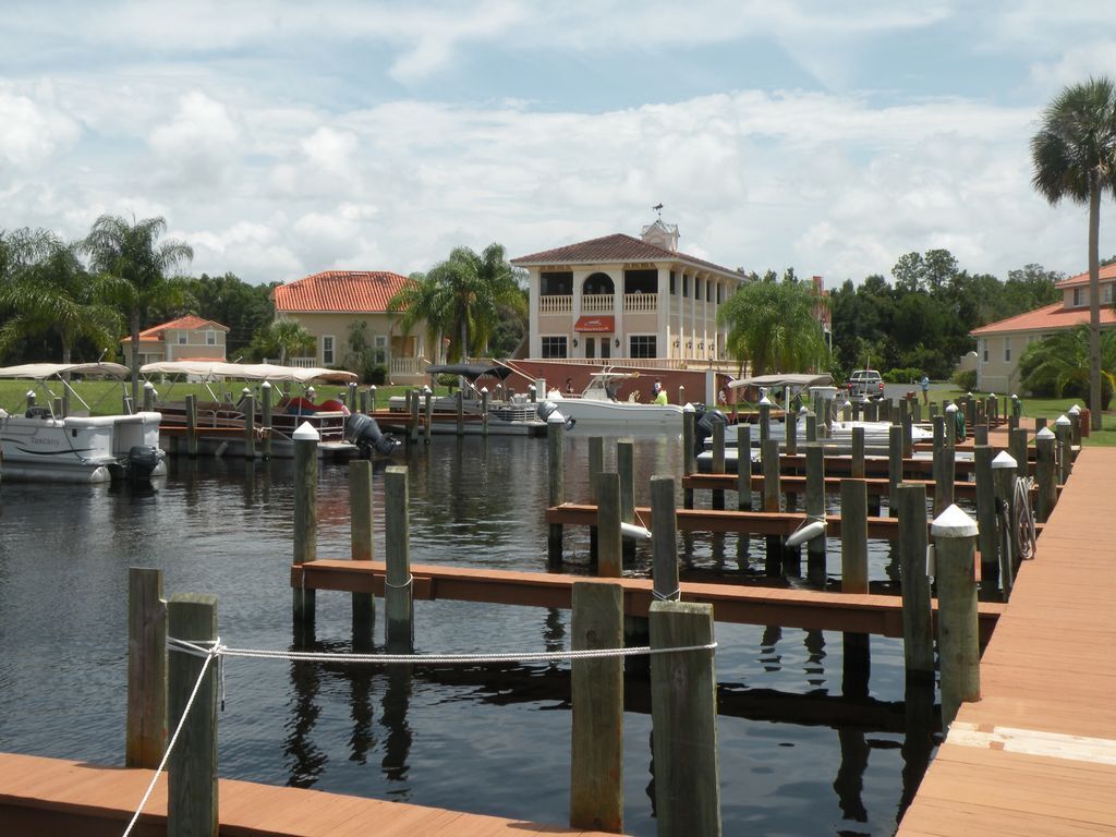 A marina with docked boats, a wooden walkway, and a building with a red roof in the background.