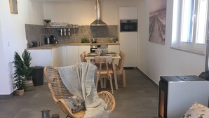 En moderne stue med sofa, spiseområde med bord og stole, køkken med komfur og skabe, samt et stort vindue.