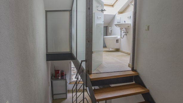 A modern staircase with wooden steps and metal railings leading to a second-floor area with a skylight and a bathroom. - Nengshof - Haus Gänseblümchen (Wissmannsdorf)