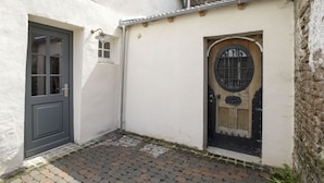 A narrow alleyway with a white wall, a grey door, and a wooden door with a metal grille. - Nengshof - Haus Gänseblümchen (Wissmannsdorf)