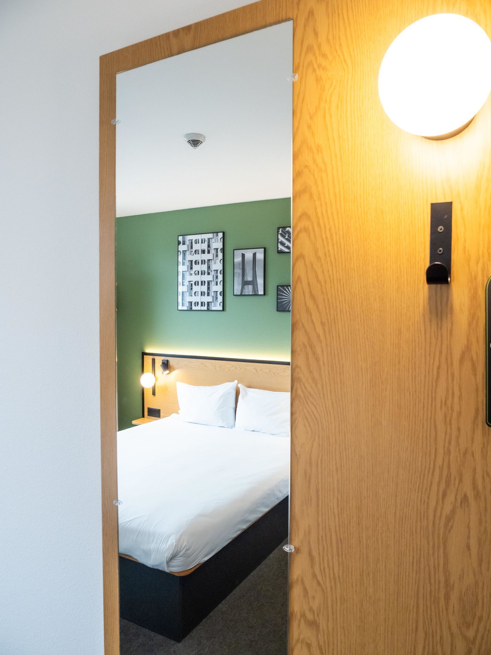 A hotel room with a bed, a green wall, and a ceiling light.