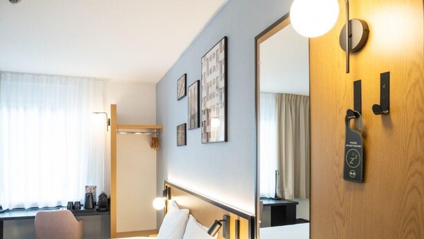 A hotel room with a bed, bedside table, lamp, mirror, and a door with a 'Do Not Disturb' sign. - Hotel B&B Wrocław Centrum (Wroclaw)