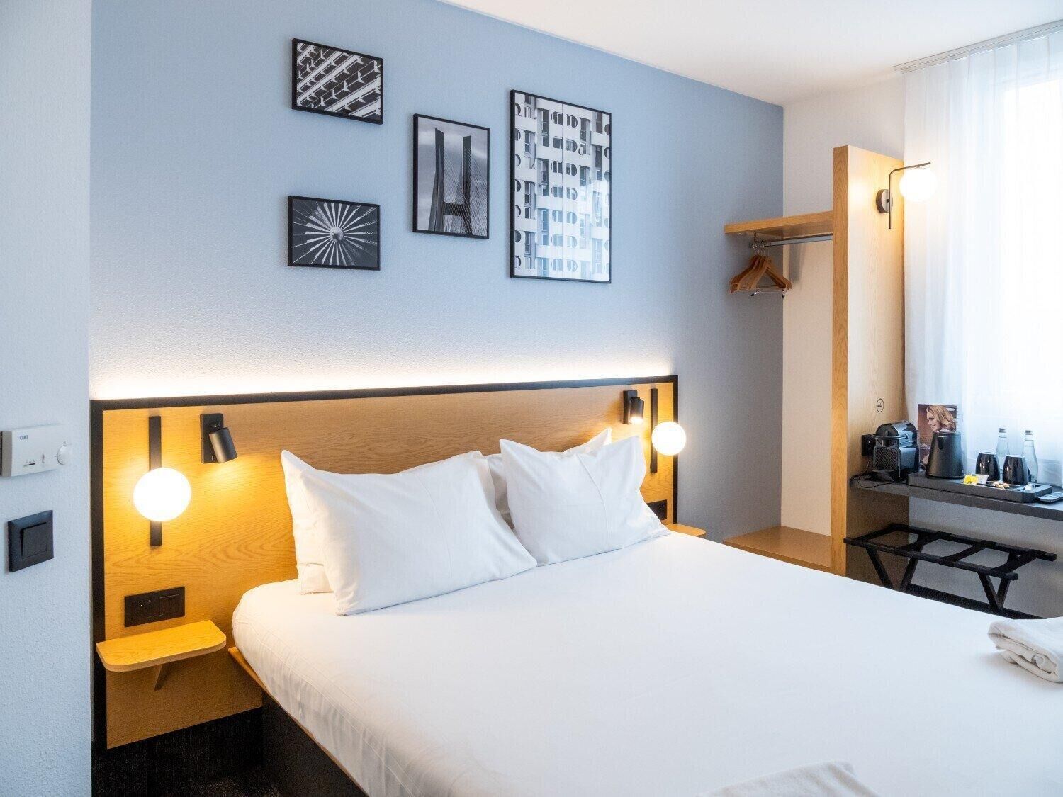 Hotellihuone, jossa on sänky, yöpöydät, työpöytä ja peili.