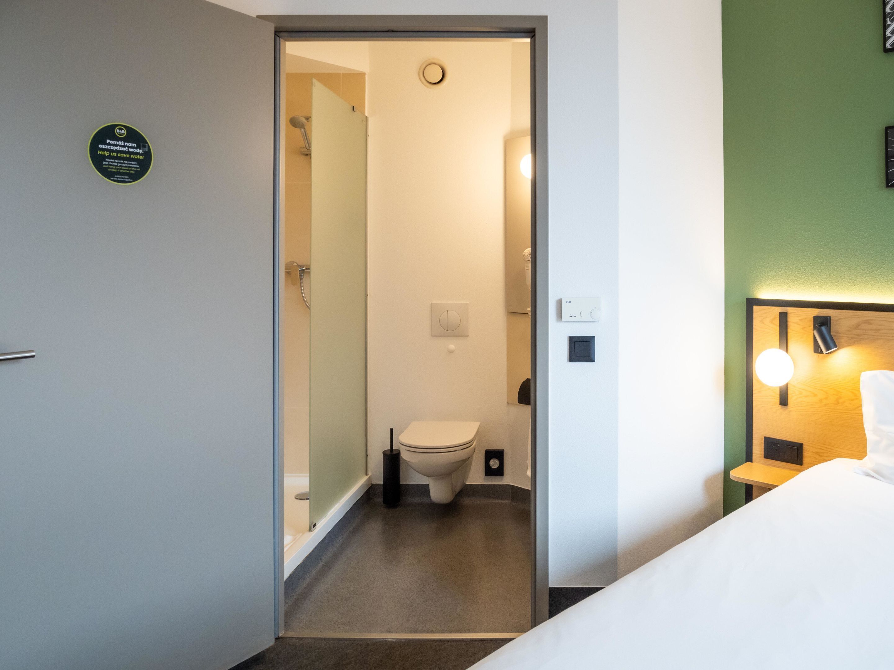 A hotel bathroom with a shower, toilet, and a visible water conservation sign.