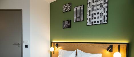 Una cama bien hecha con sábanas blancas, un cabecero de madera y dos mesitas de noche con lámparas de pared.