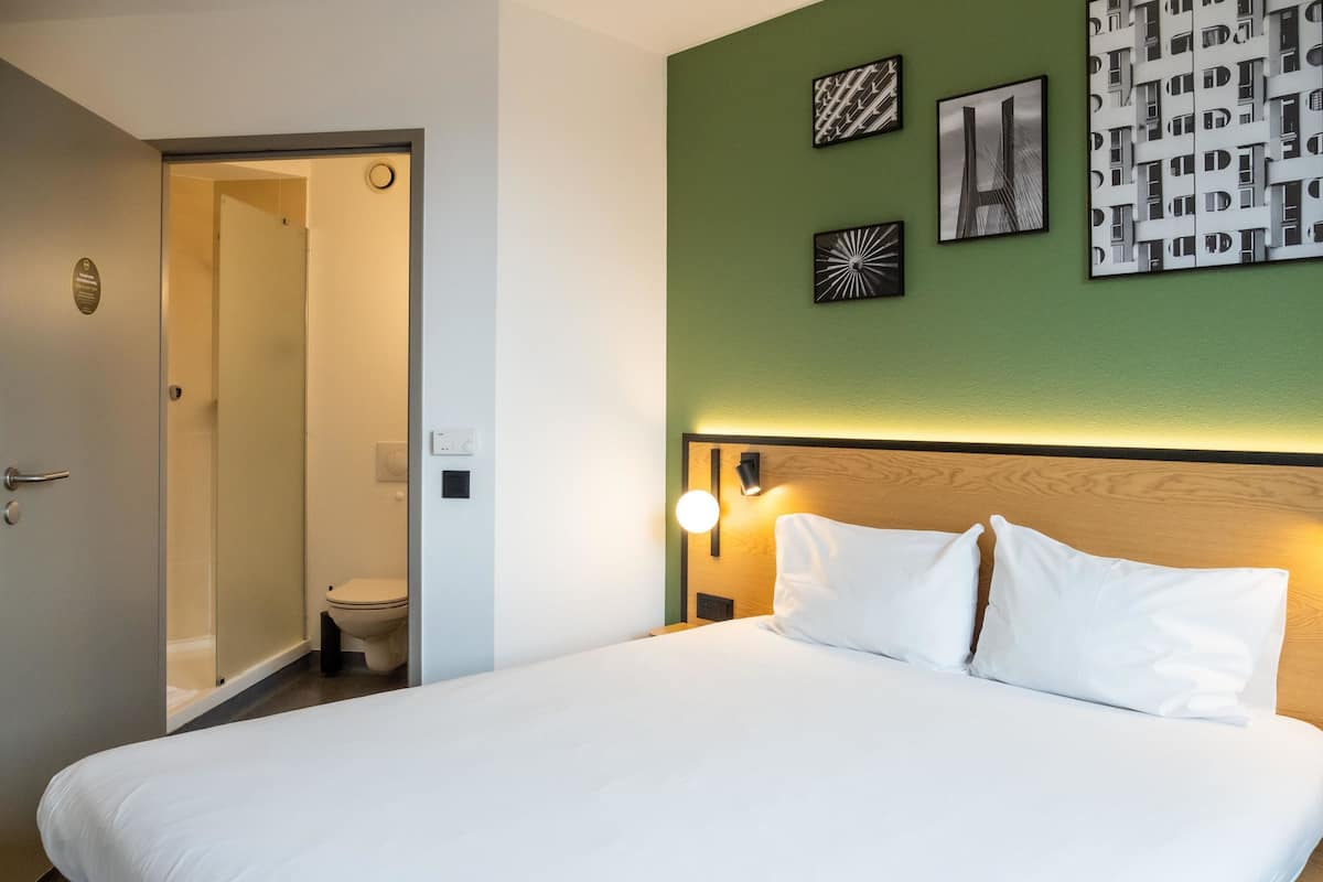 A hotel room with a bed, a door leading to a bathroom, and a green wall with three framed pictures.