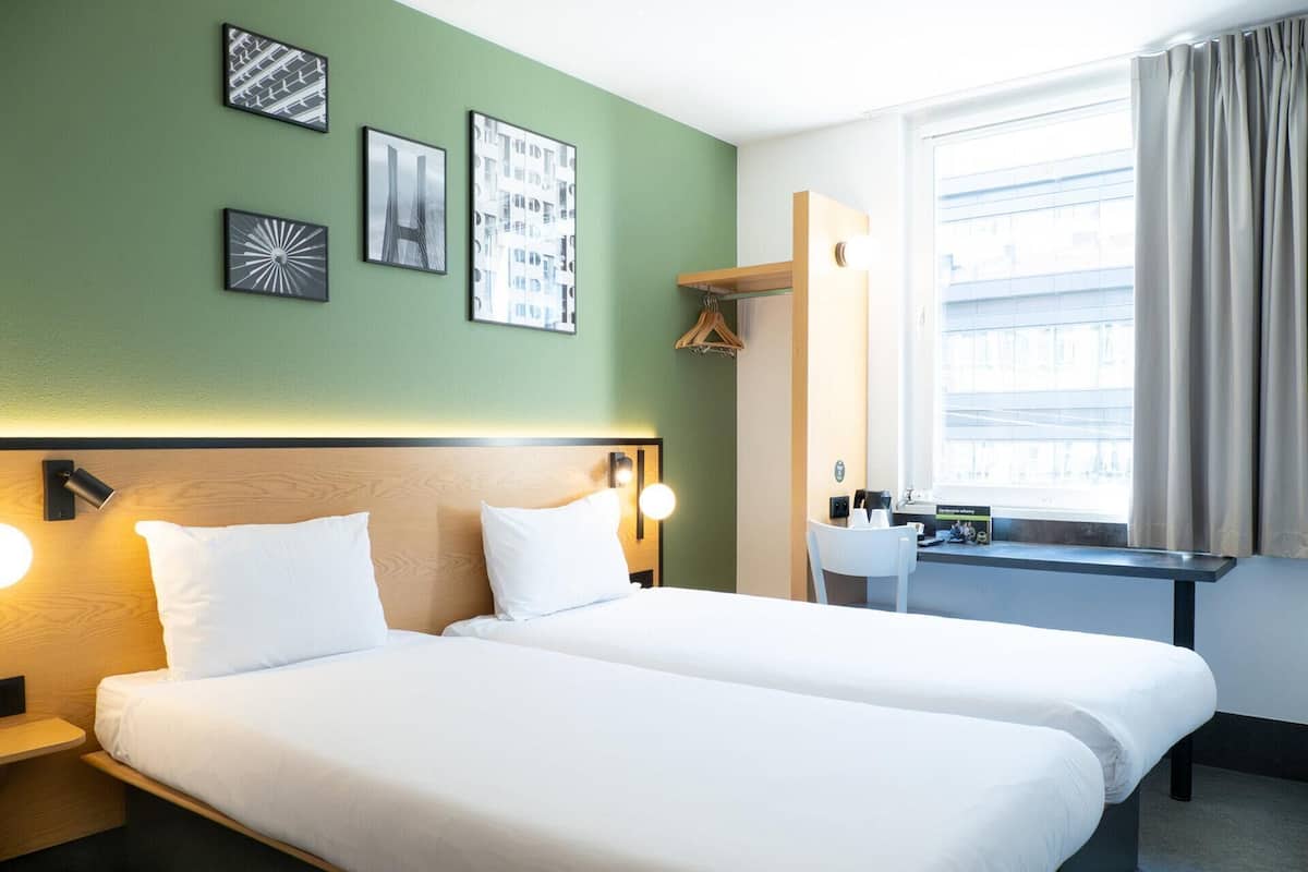 A hotel room with two beds, a desk, a chair, and a window with curtains.