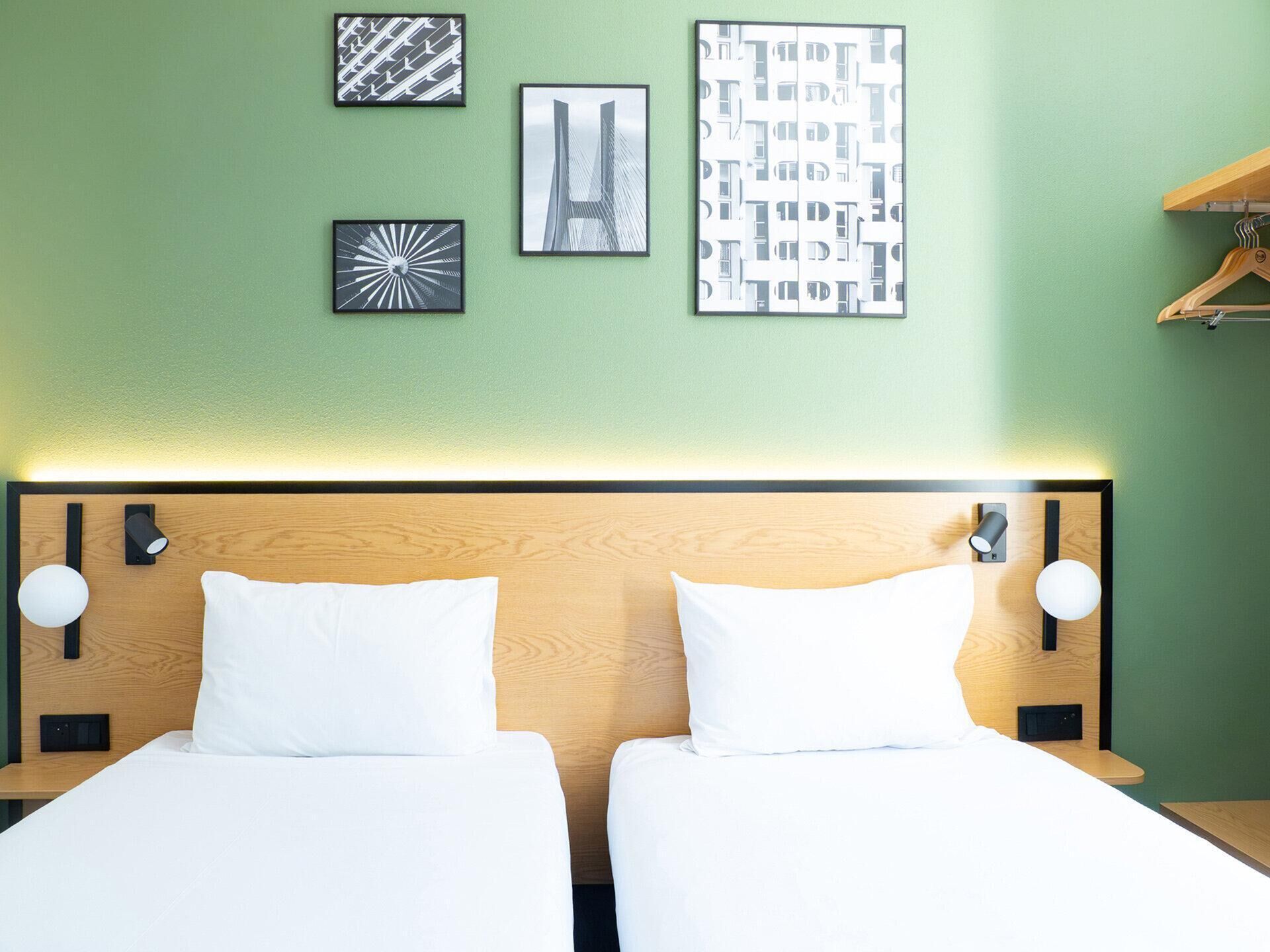 Una habitación de hotel con dos camas, cabecero de madera y obras de arte colgadas en la pared.