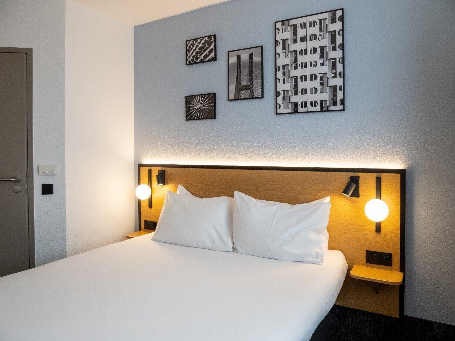 A hotel room with a large bed, two bedside tables with lamps, and three wall art pieces.