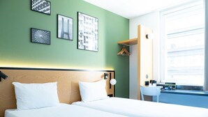 A hotel room with two beds, a small desk, a chair, a window, and artwork on the wall. - Hotel B&B Wrocław Centrum (Wroclaw)