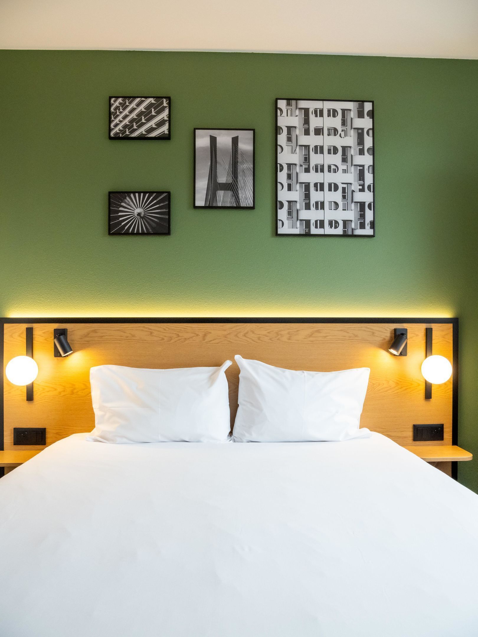Una camera d'albergo con un letto, due lampade da comodino e tre quadri appesi al muro.