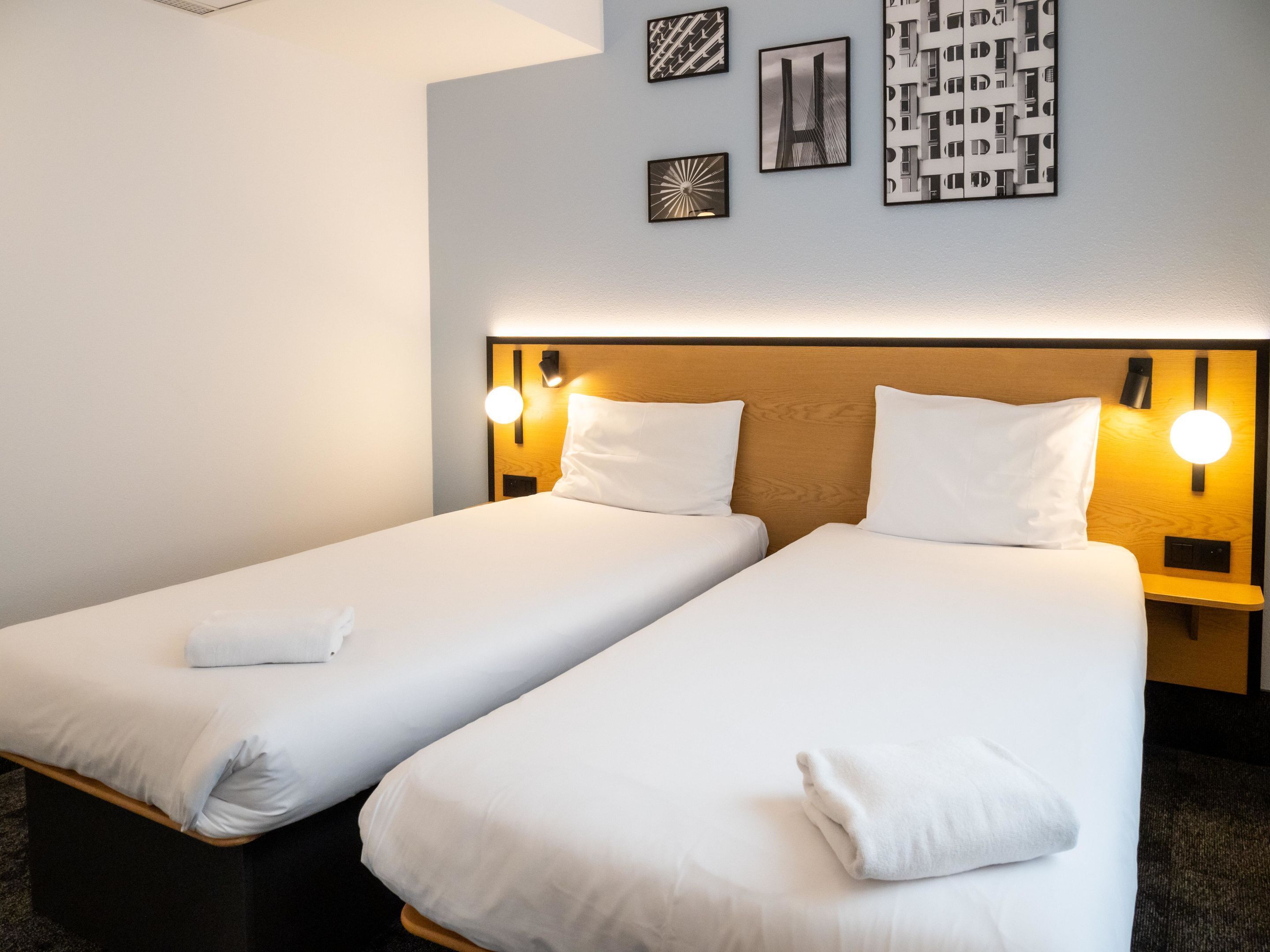 A hotel room with two single beds, each with a wooden headboard and bedside lamps.
