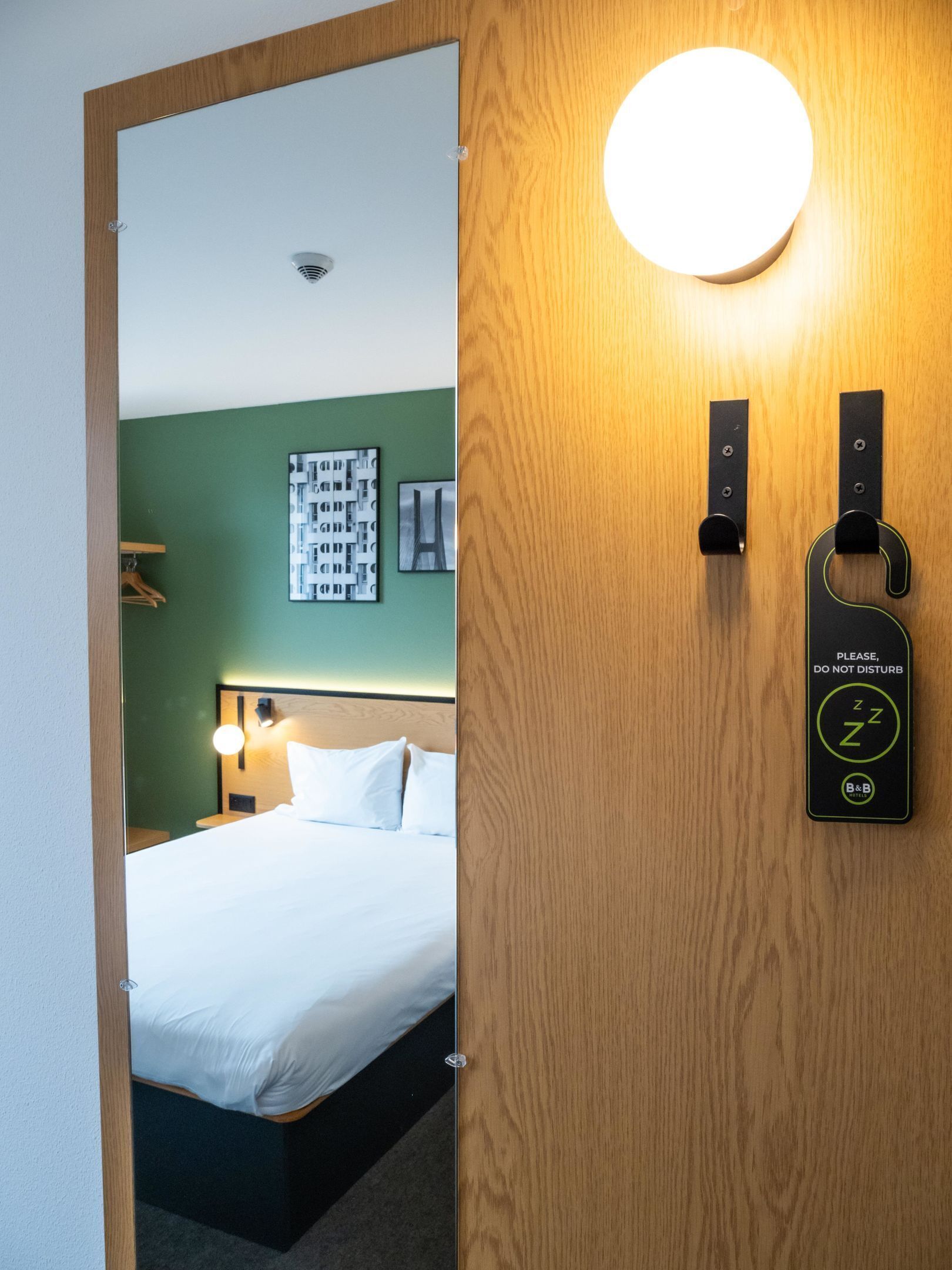 Une chambre d’hôtel avec un lit, une table de chevet, une lampe fixée au mur et une porte sur laquelle est apposée une pancarte indiquant : « Veuillez ne pas déranger ».