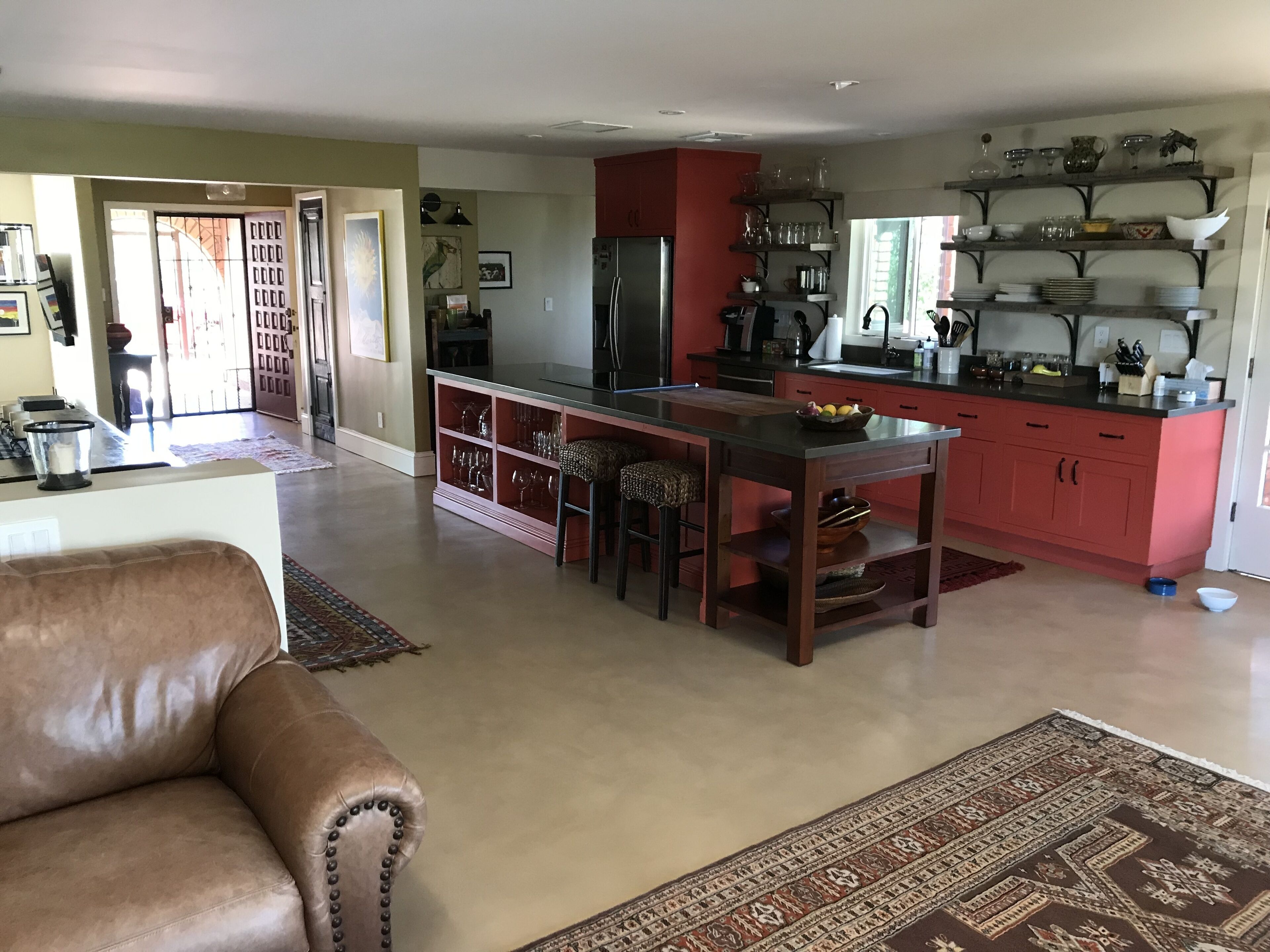 A spacious living area with a leather sofa, a kitchen with red cabinets, and a dining area with stools.
