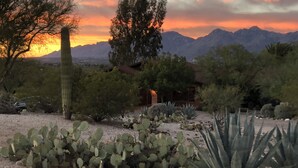 A desert landscape with cacti and a house with a red roof, surrounded by mountains and a sunset sky. - Tucson Gem in the Heart of the Desert (Tucson)