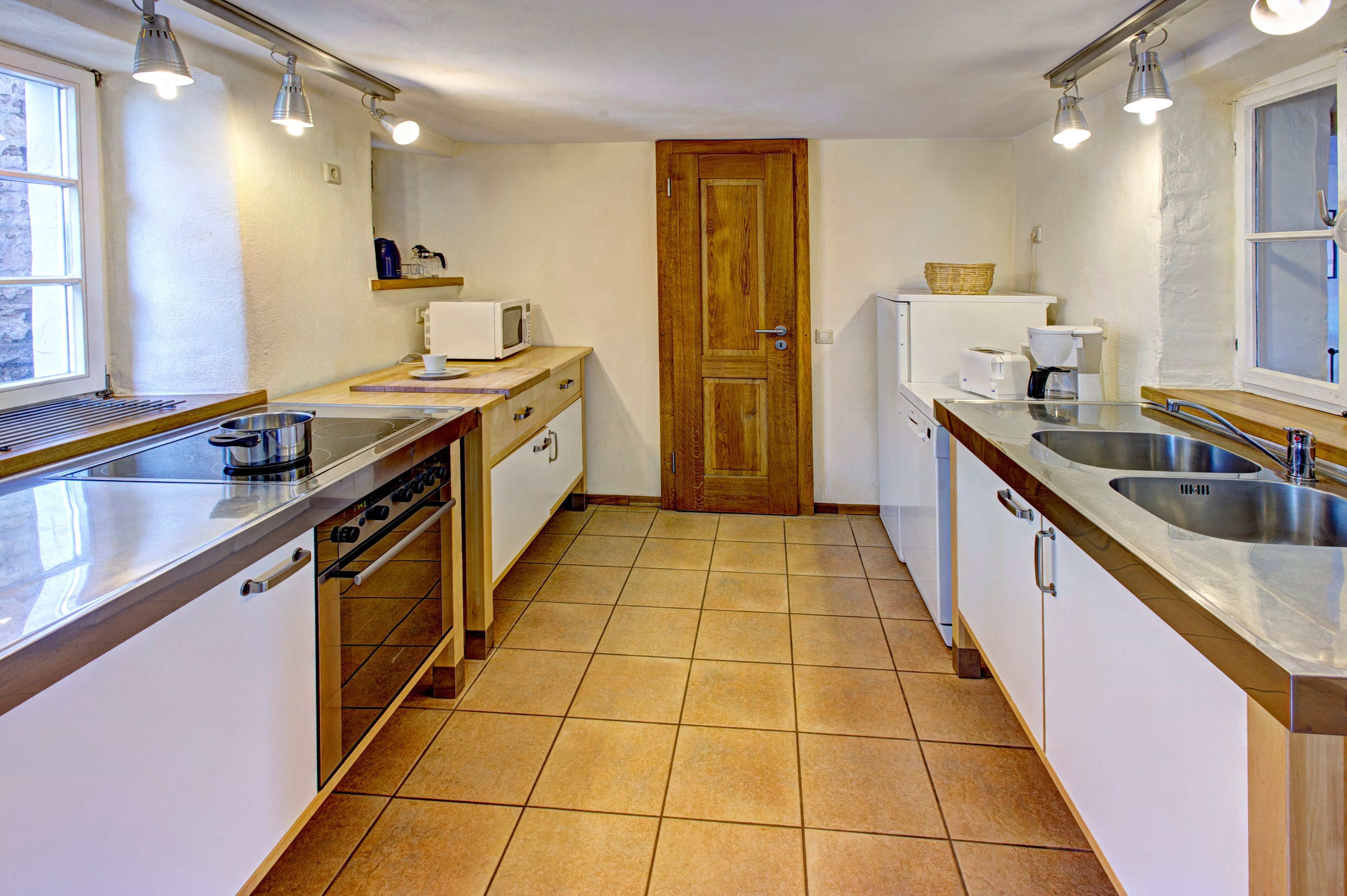 Una cucina compatta con fornelli, forno a microonde e lavello, pensili in legno e pavimento piastrellato.