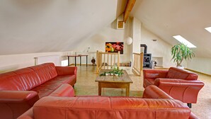 A spacious living room with a high ceiling and skylights, featuring a red leather sofa set, a wooden coffee table, and a bookshelf. - Nengshof - Haus Königskerze (Wissmannsdorf)