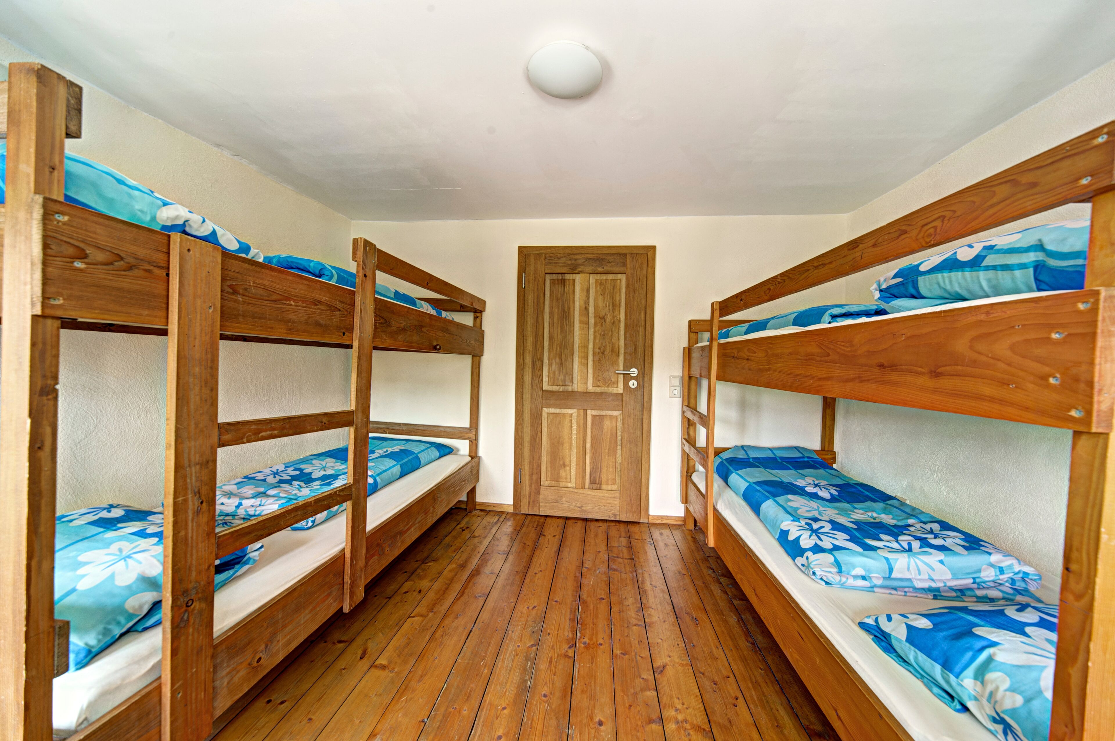 A room with three bunk beds, wooden flooring, and a door in the center.