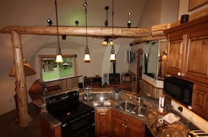 Una cocina con armarios de madera, encimera de granito, estufa e iluminación colgante.