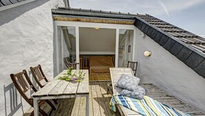A wooden deck with a table and chairs, a sofa with cushions, and a sliding glass door leading to an interior space. - Nengshof - Haus Ehrenpreis (Wissmannsdorf)