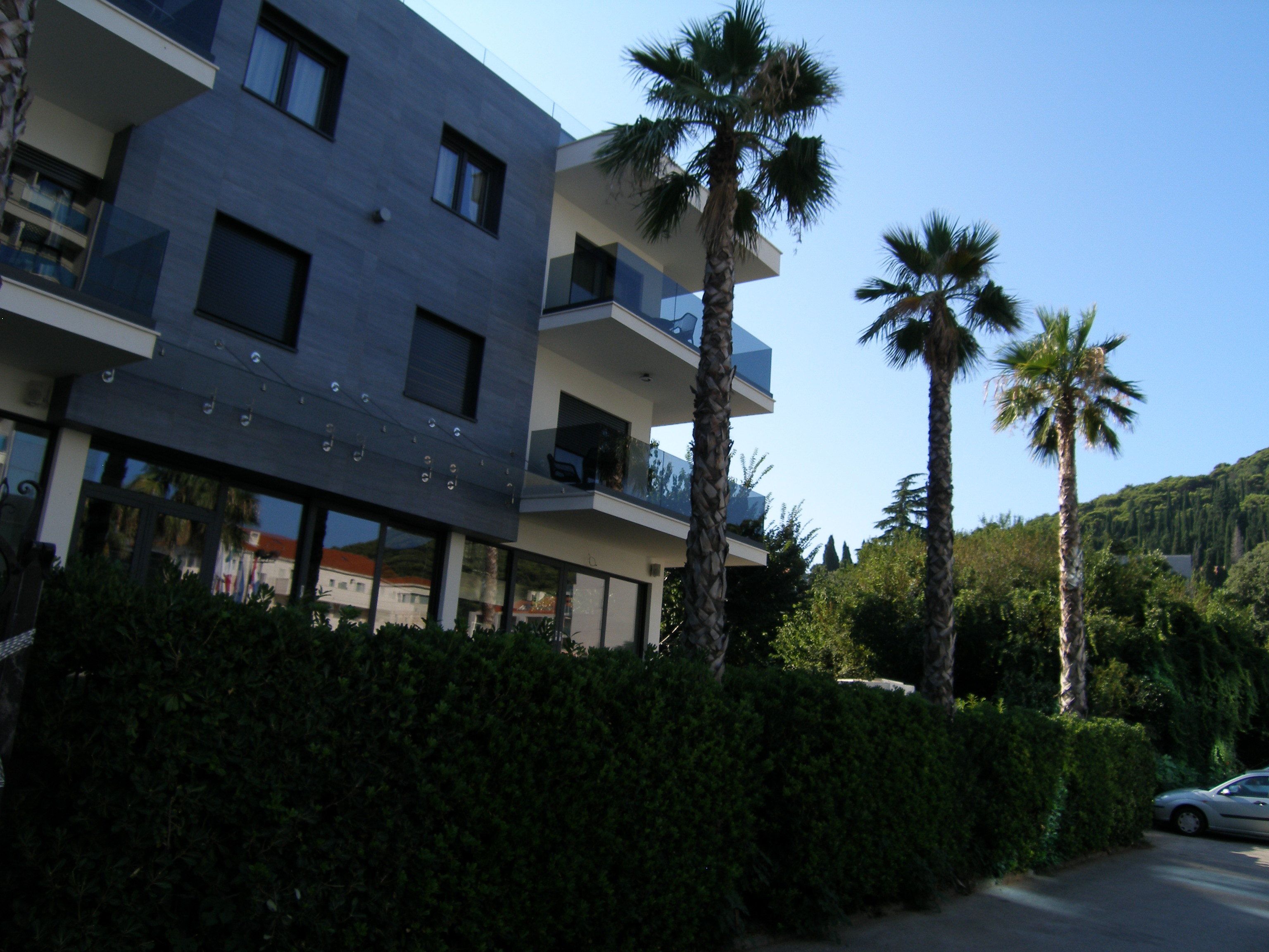 Un immeuble moderne à plusieurs étages, doté de balcons, entouré d’une végétation luxuriante et de palmiers.