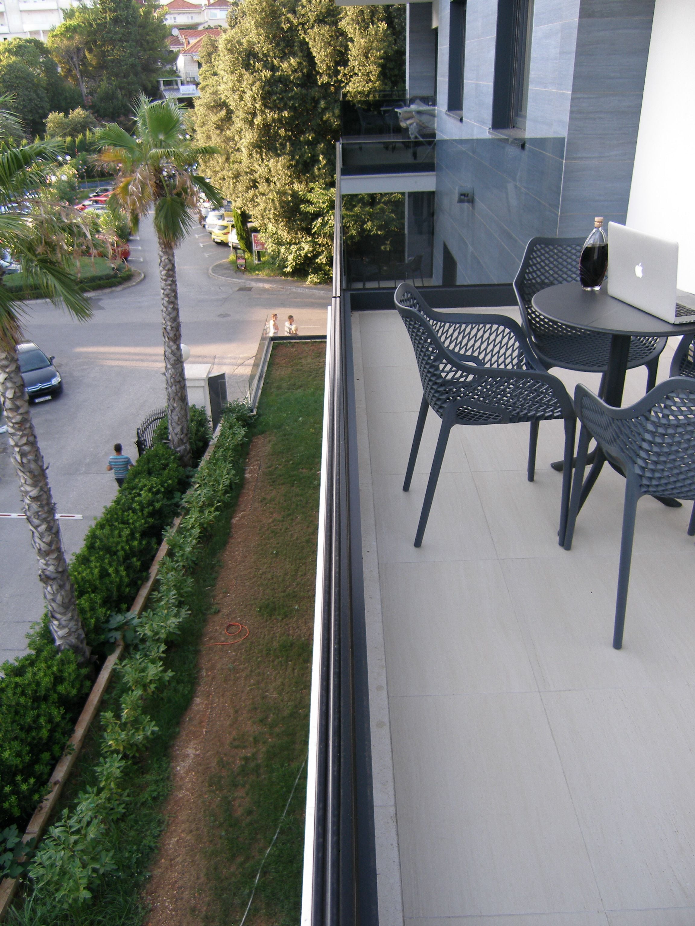 A balcony with a table and chairs, overlooking a street with cars and trees.