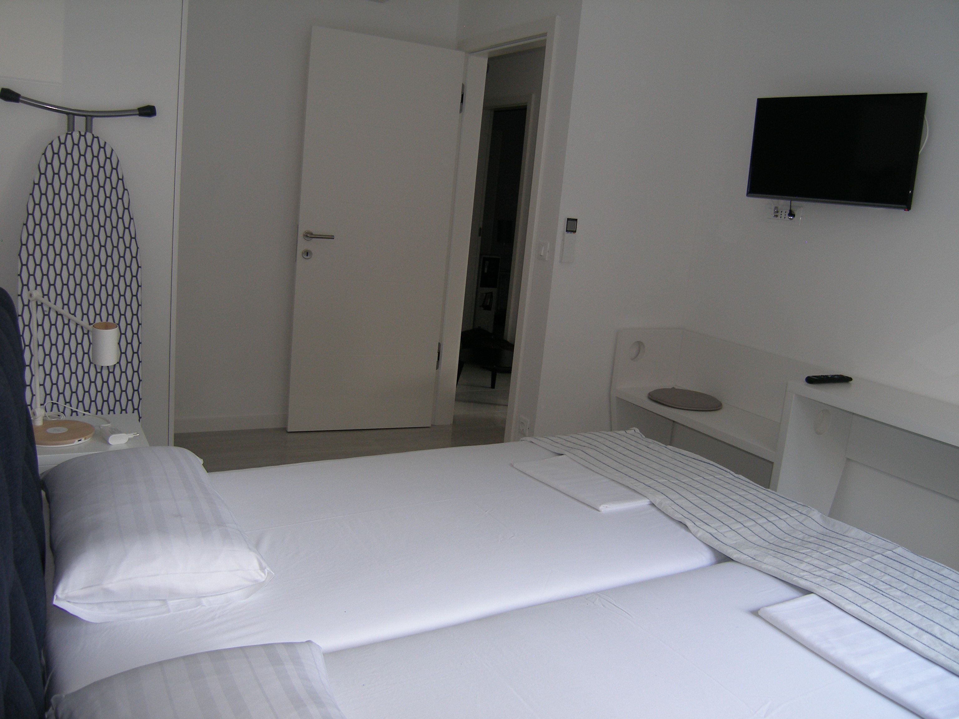A hotel room with a bed, a TV mounted on the wall, a door, and a small table with a lamp.