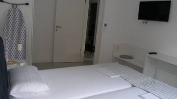 A hotel room with a bed, a TV mounted on the wall, a door, and a small table with a lamp.