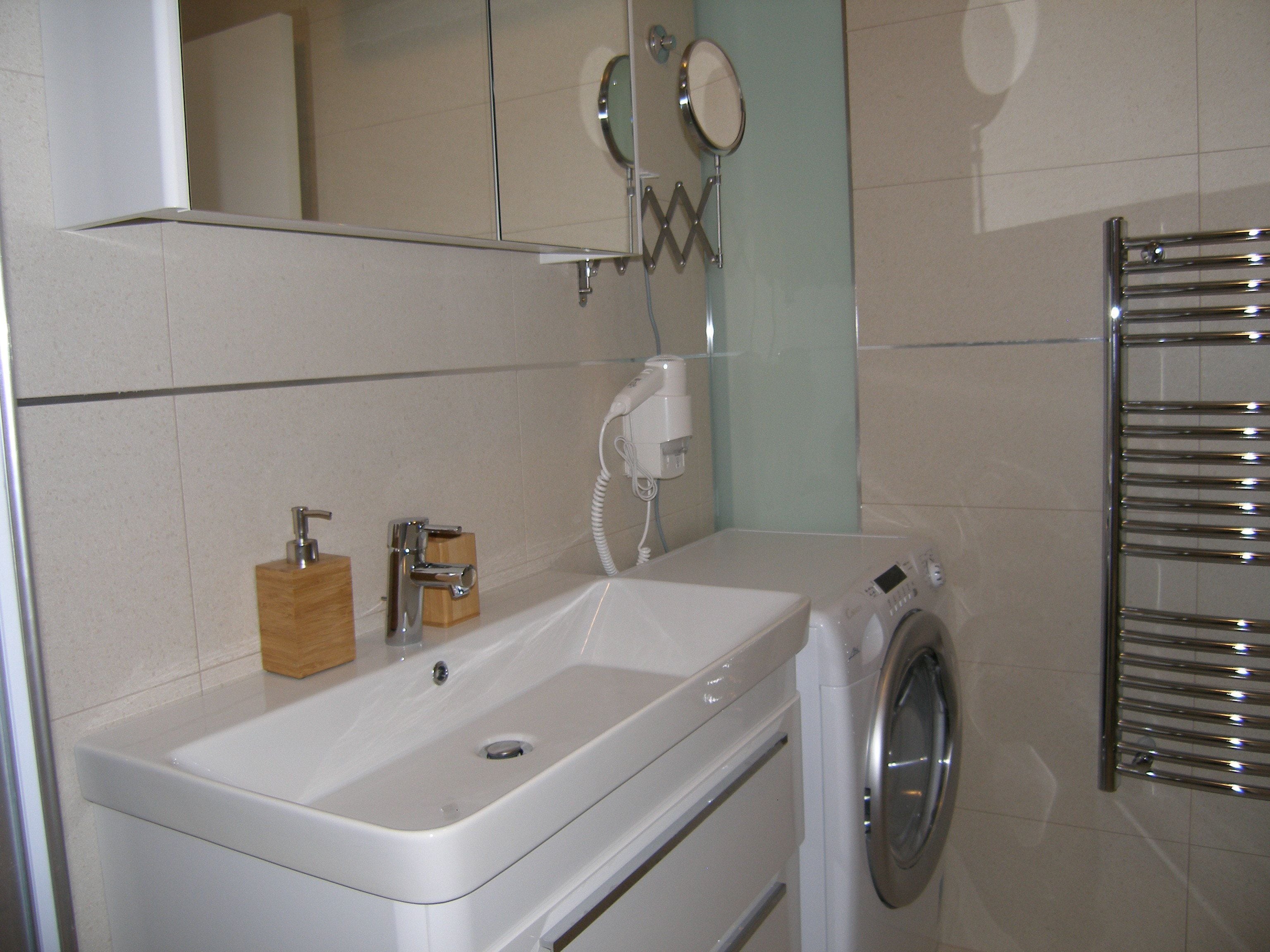 Een badkamer met een wastafel, spiegel en wasmachine.